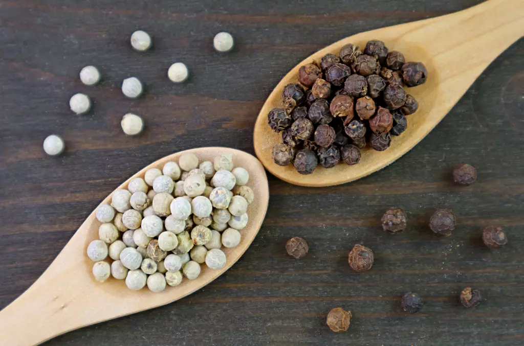 vue-de-dessus-des-cuilleres-de-grains-de-poivre-blanc-et-de-grains-de-poivre-noir-sur-fond-de-bois-noir